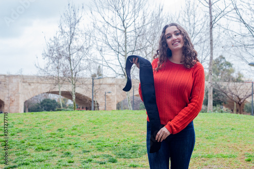 Portrait of attractive caucasian young woman holding electronic abdominal appliance, in the park, orange sweater and jeans. Place for your text in copy space.