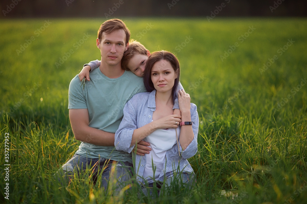 Classic happy modern young family is sitting in a park on green grass. Three: mom dad son. Parenthood A walk in the garden on the nature outside. Calm pacific mother father. Love togetherness. Summer Classic happy modern young family is sitting in a park on green grass. Three: mom dad son. Parenthood A walk in the garden on the nature outside. Calm pacific mother father. Love togetherness. Summer