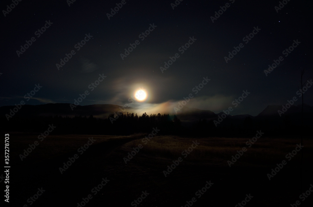 dreamy full moon night sky over field, forest road and mountain