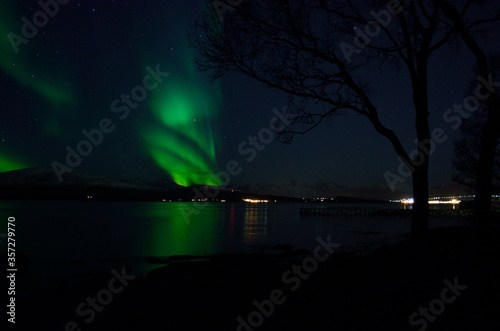 vibrant aurora borealis over fjord and mountain reflecting on fjord surface at night