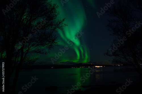 vibrant aurora borealis over fjord and mountain refleting in sea surface