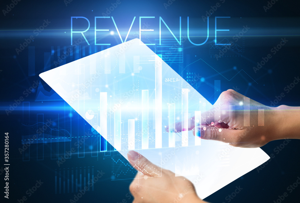 Hand holding futuristic tablet with REVENUE inscription above, modern business concept Hand holding futuristic tablet with REVENUE inscription above, modern business concept
