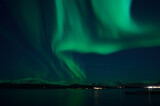 incredible strong aurora borealis over fjord and snowy mountain