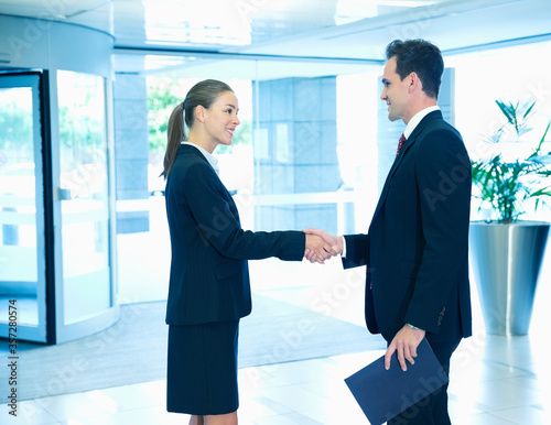 Smiling businessman and businesswoman handshaking in lobby