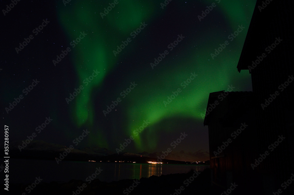 aurora borealis over mountain and fjord with boathouse