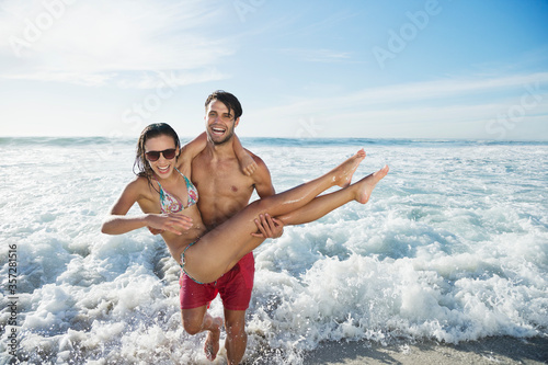 Enthusiastic man carrying woman on beach photo