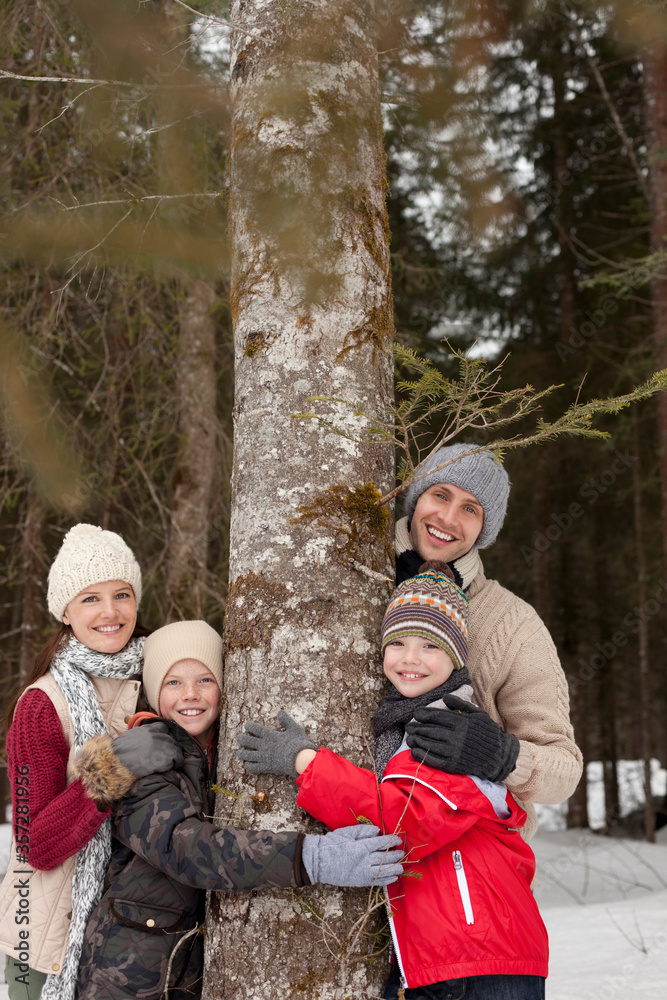 Portrait of happy family hugging tree trunk in snowy woods