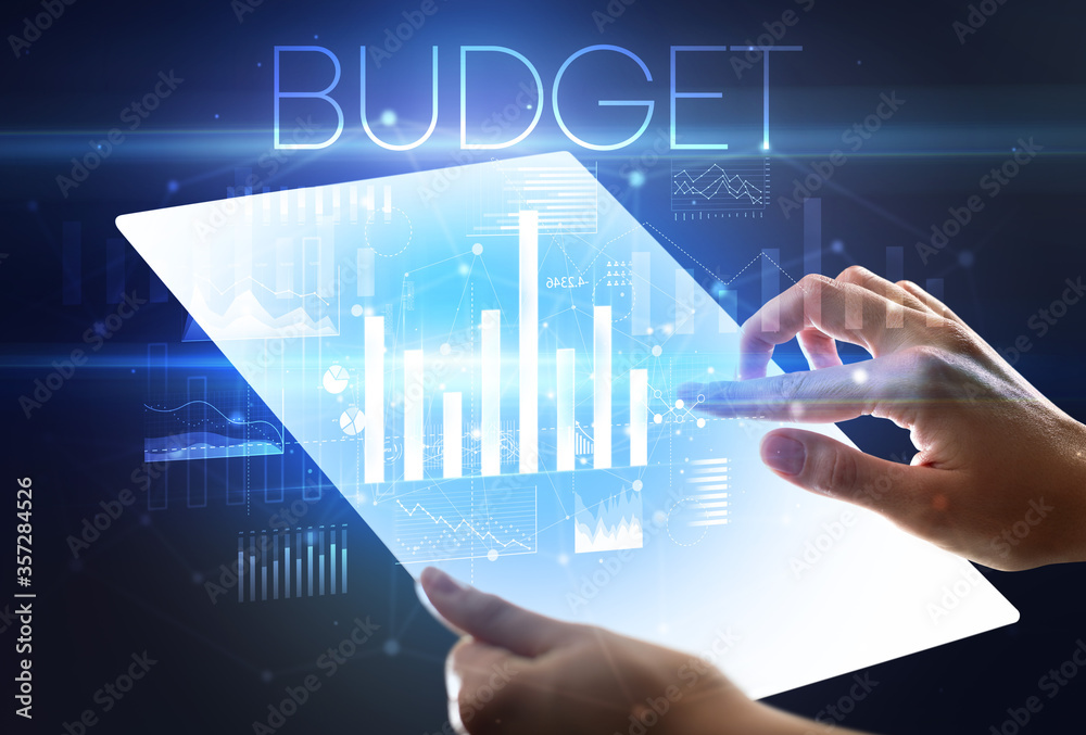 Hand holding futuristic tablet with BUDGET inscription above, modern business concept Hand holding futuristic tablet with BUDGET inscription above, modern business concept