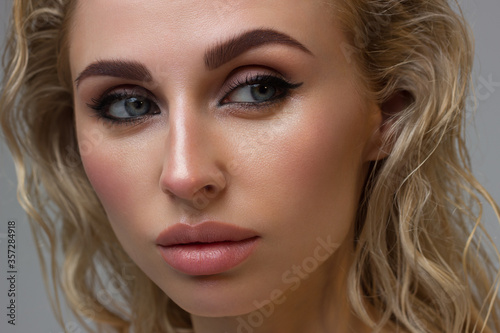 Beautiful woman with bright make up eye with sexy black liner makeup. Fashion big arrow shape on woman's eyelid. Natural lips. Chic evening make-up. Blonde long wave hair. Shining face skin