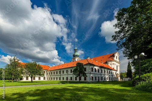 Brevnov, Prague / Czech Republic - June 11 2020: View of the first male monastery in Bohemia standing in a park with green trees on a sunny summer day, blue sky with white clouds. photo