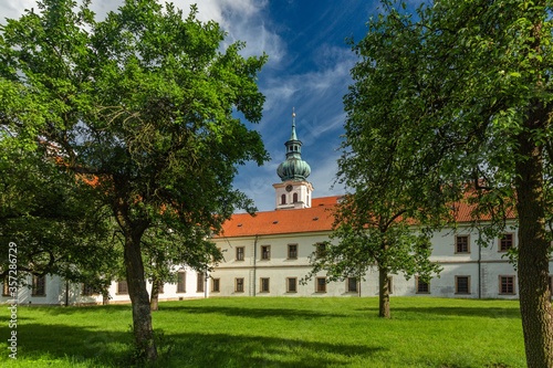 Brevnov, Prague / Czech Republic - June 11 2020: View of the first male monastery in Bohemia standing in a park with green trees on a sunny summer day, blue sky with white clouds. photo