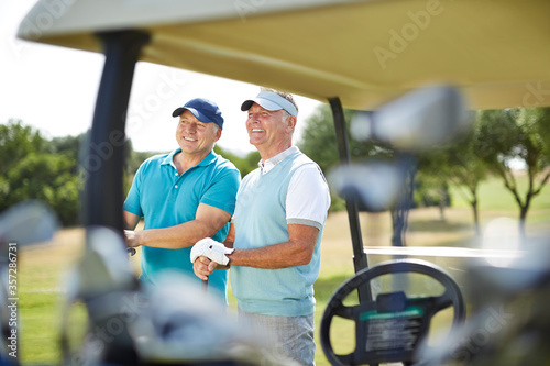 Senior men standing next to golf cart
