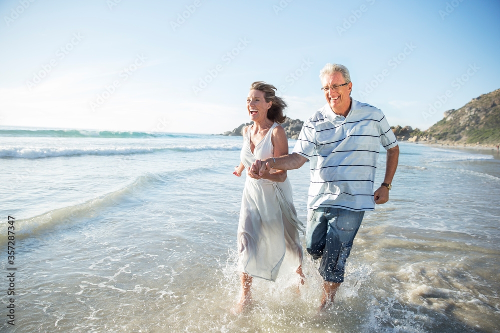 Fototapeta premium Older couple playing in waves on beach