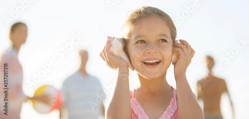 Obraz na plátně Girl listening to conch shells on beach