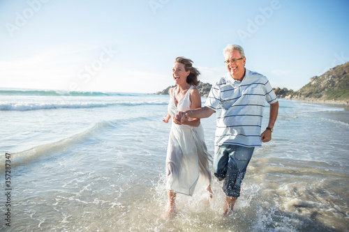 Fotografi Older couple playing in waves on beach