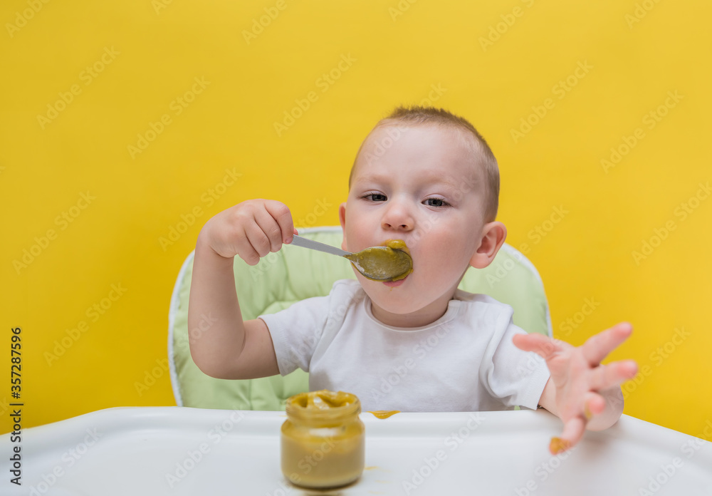 Portrait of a Small boy sitting in a chair and learning to eat broccoli puree on a yellow isolated background with space for text Portrait of a Small boy sitting in a chair and learning to eat broccoli puree on a yellow isolated background with space for text