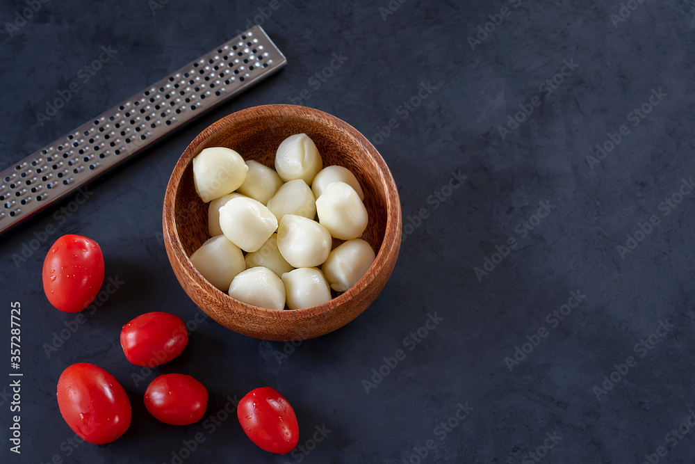 Scamorza cheese in a bowl with grater and cherry tomatoes on a black background. Scamorza cheese in a bowl with grater and cherry tomatoes on a black background.