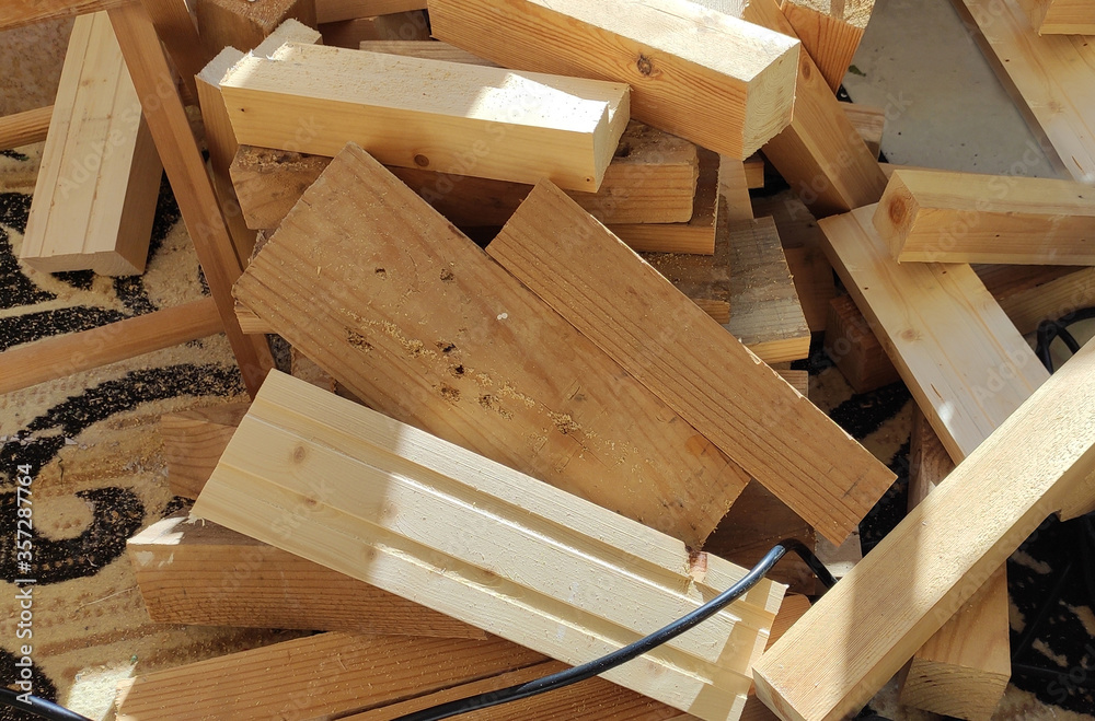 Lumber. Firewood. Building materials for construction on the floor. Sawn wooden boards, bars on a sawmill close-up. Electro instrument, fret saw on chair.