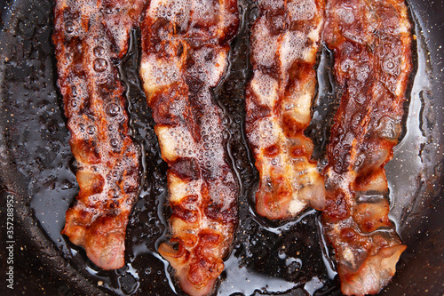 Crispy smokey bacon slice or strip. Unhealthy fat food, fattenig ingredient. Red Thin slice or strip or rashers of bacon is fried in a pan, pork fat is melted. High calorie food. Idea for breakfast