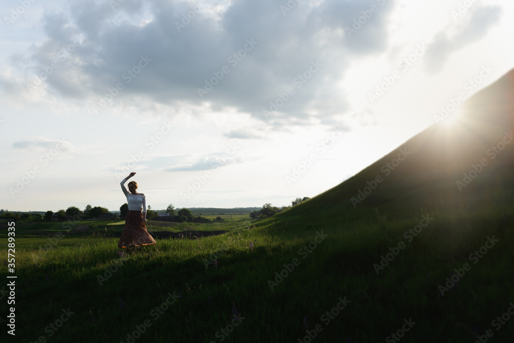 Young happy girl is dancing at sunset with raised arms. High quality photo