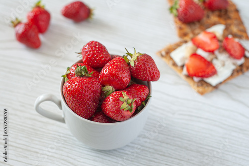 Strawberries in a cup on a light wooden background. Biscuits with cheese  strawberries and hazelnuts. Dietary nutrition. Summer breakfast. A healthy snack.