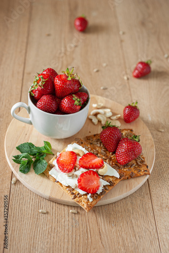 A healthy light breakfast with strawberries  cream cheese  nuts and seeds. On a wooden background in warm tones. Strawberries in a cup and mint leaves.