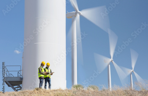 Workers talking by wind turbines in rural landscape