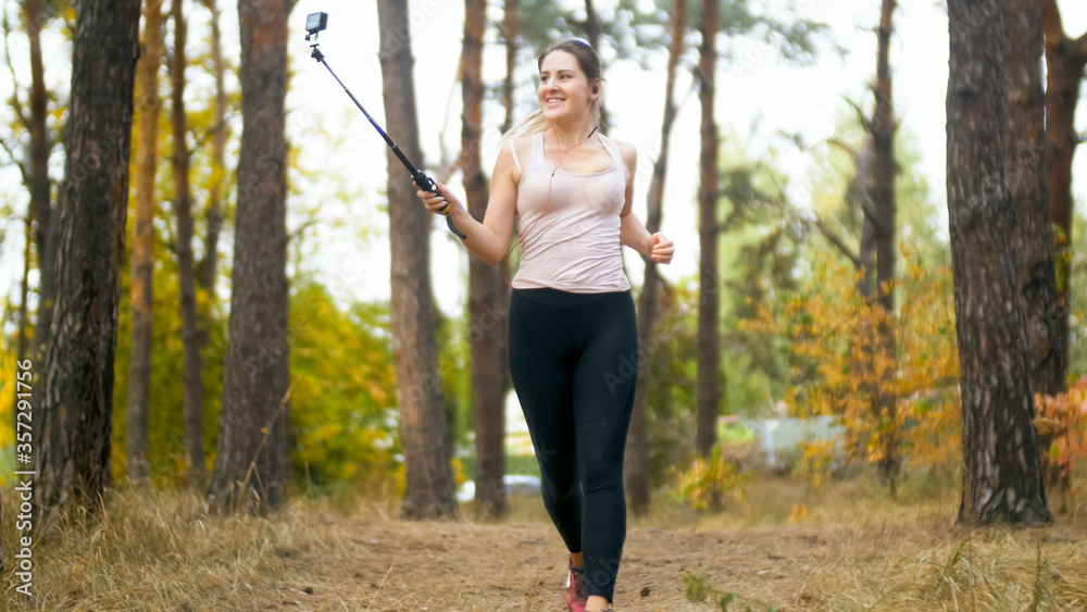 Smiling young woman making selfie photo on smartphone while running in forest Smiling young woman making selfie photo on smartphone while running in forest