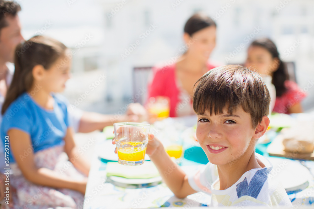 Boy drinking juice at table on sunny patio Boy drinking juice at table on sunny patio