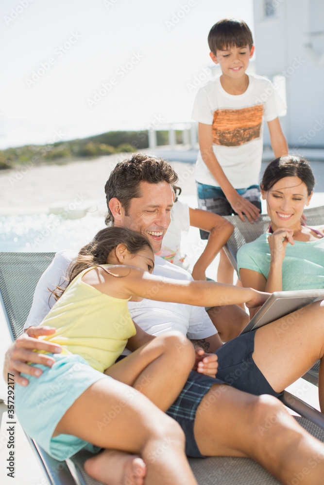 Family using digital tablet on lounge chairs at poolside Family using digital tablet on lounge chairs at poolside