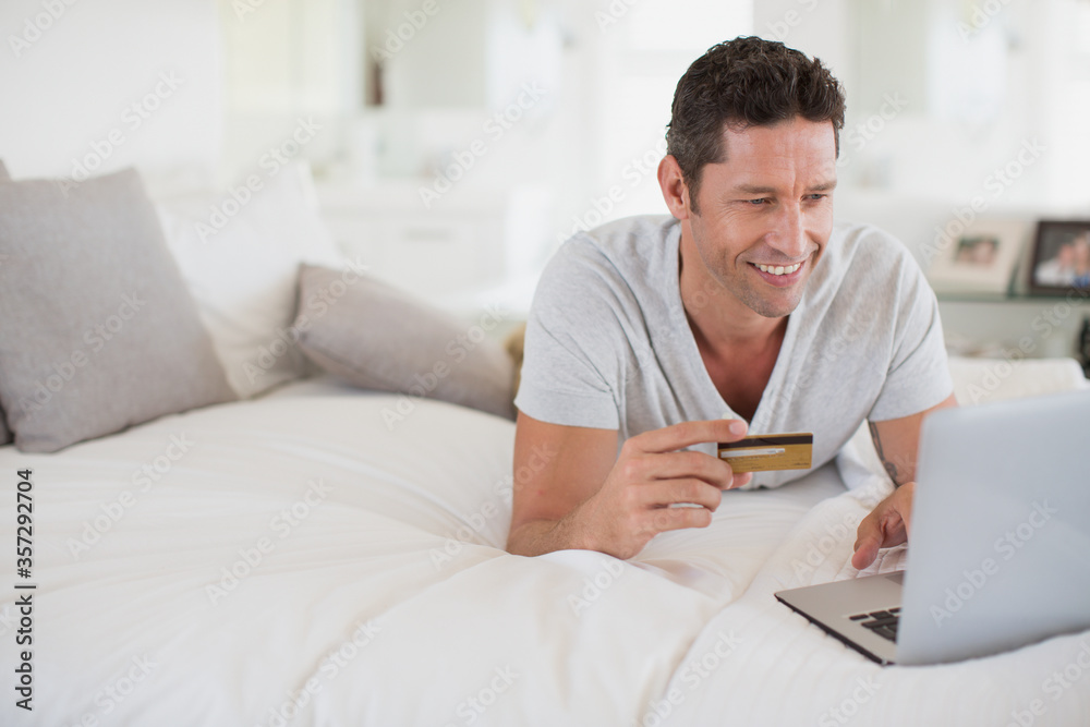 Man shopping online with laptop on bed Man shopping online with laptop on bed