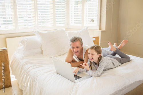 Father and daughter using laptop on bed © Chris Ryan/KOTO