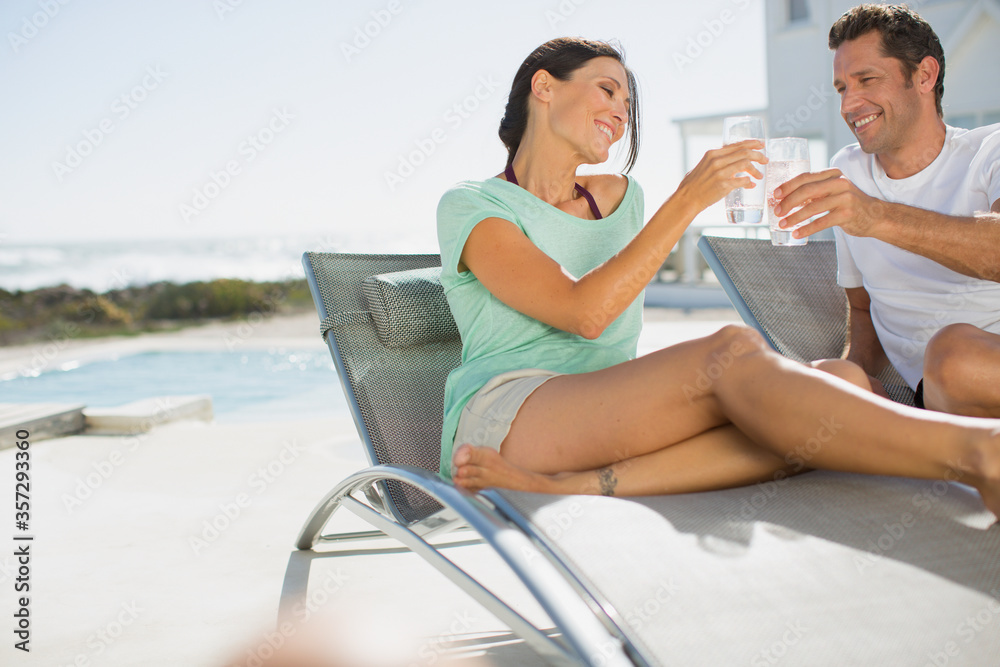 Couple toasting water glasses in lounge chairs at poolside
