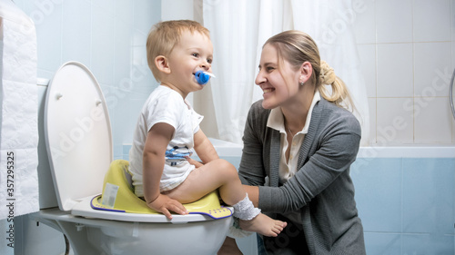 Cute little boy smiling to mother while sitting on toilet seat photo