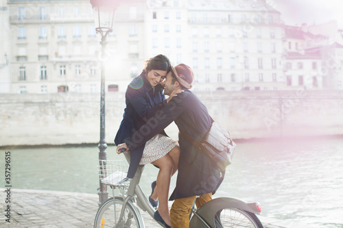 Photography Couple hugging on bicycle along Seine River, Paris, France