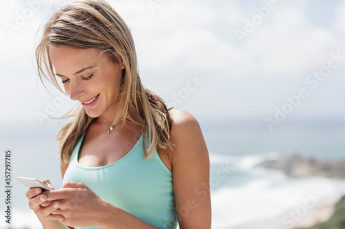 Smiling woman texting with cell phone in front of ocean