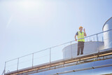 Worker using walkie-talkie on platform next to silage storage towers