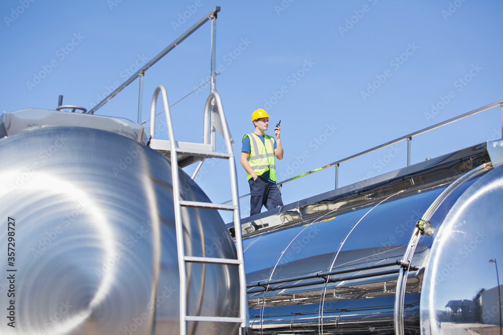 Worker using walkie-talkie on platform above stainless steel milk tanker Worker using walkie-talkie on platform above stainless steel milk tanker