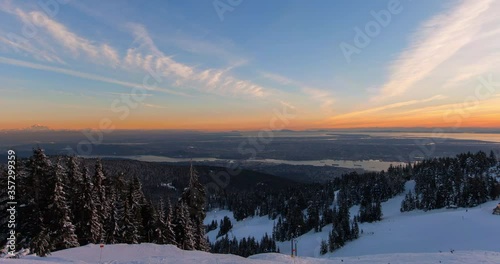 Lockdown time lapse shot of people skiing on snowcapped mountain by city against sky during sunset - Vancouver, Canada photo