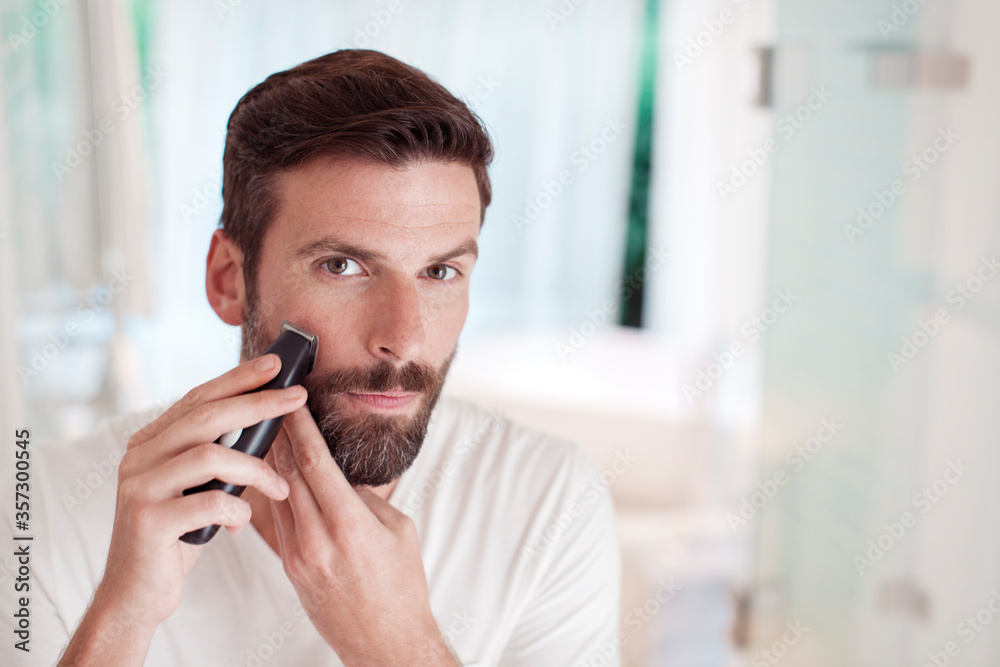 Man trimming beard in bathroom mirror Man trimming beard in bathroom mirror