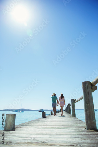 Couple holding hands walking along wooden dock