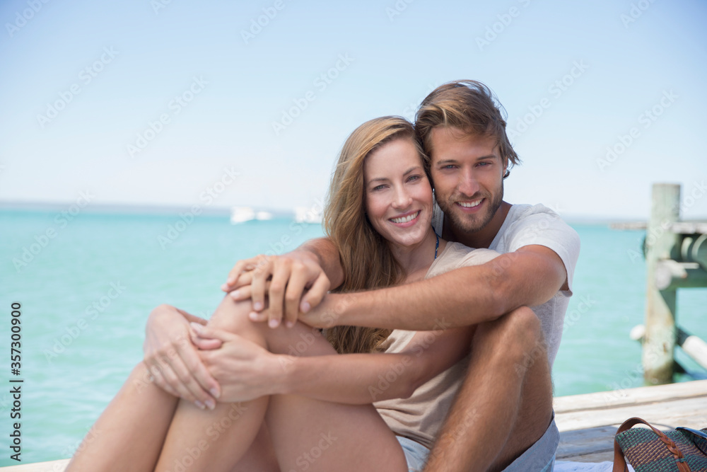 Couple sitting together on edge of wooden dock Couple sitting together on edge of wooden dock