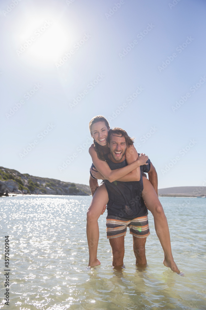Woman being carried piggy back by boyfriend in waves Woman being carried piggy back by boyfriend in waves
