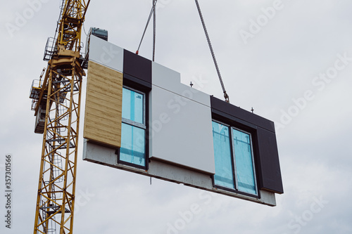 Installation of prefabricated walls at the construction site. The crane moves concrete elements