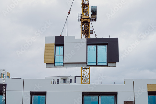 Installation of prefabricated walls at the construction site. The crane moves concrete elements photo