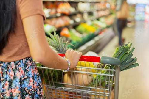 Close up of woman pushing full shopping cart in grocery store photo