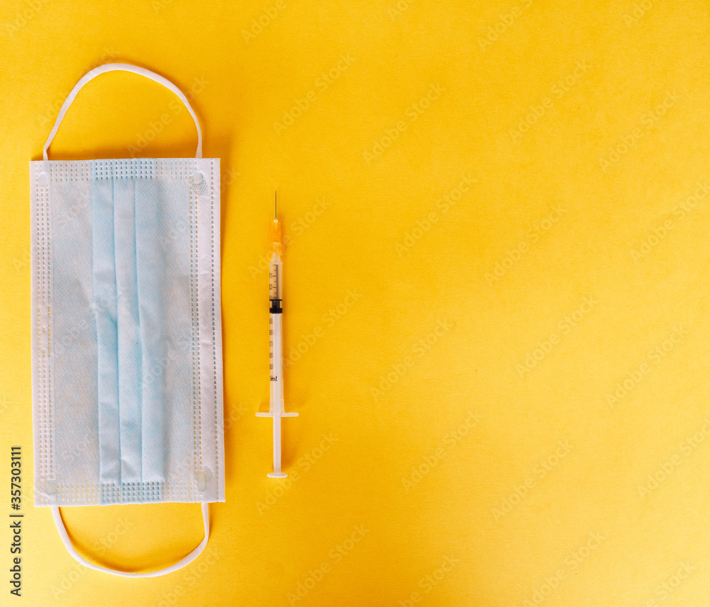 Top view of medical concept with syringe and mask on yellow background for coronavirus prevention. Covid-19 kit. Copy Space Top view of medical concept with syringe and mask on yellow background for coronavirus prevention. Covid-19 kit. Copy Space