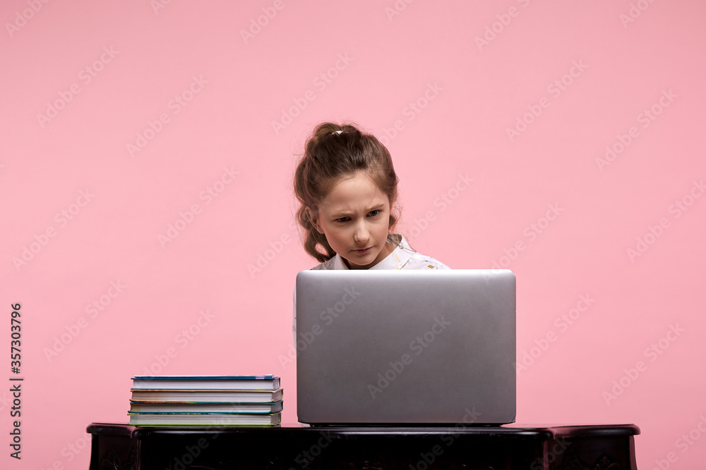 girl on a pink background sits at a table with a computer with a surprised face girl on a pink background sits at a table with a computer with a surprised face