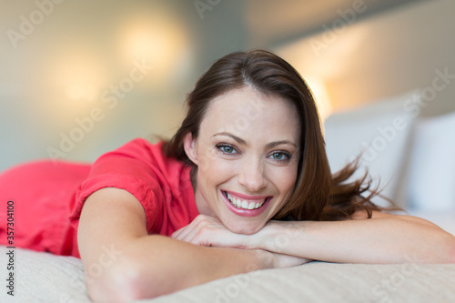 Portrait smiling mid-adult woman wearing red dress lying on bed in bedroom