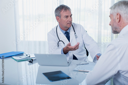 Mature doctor talking to patient at desk in office